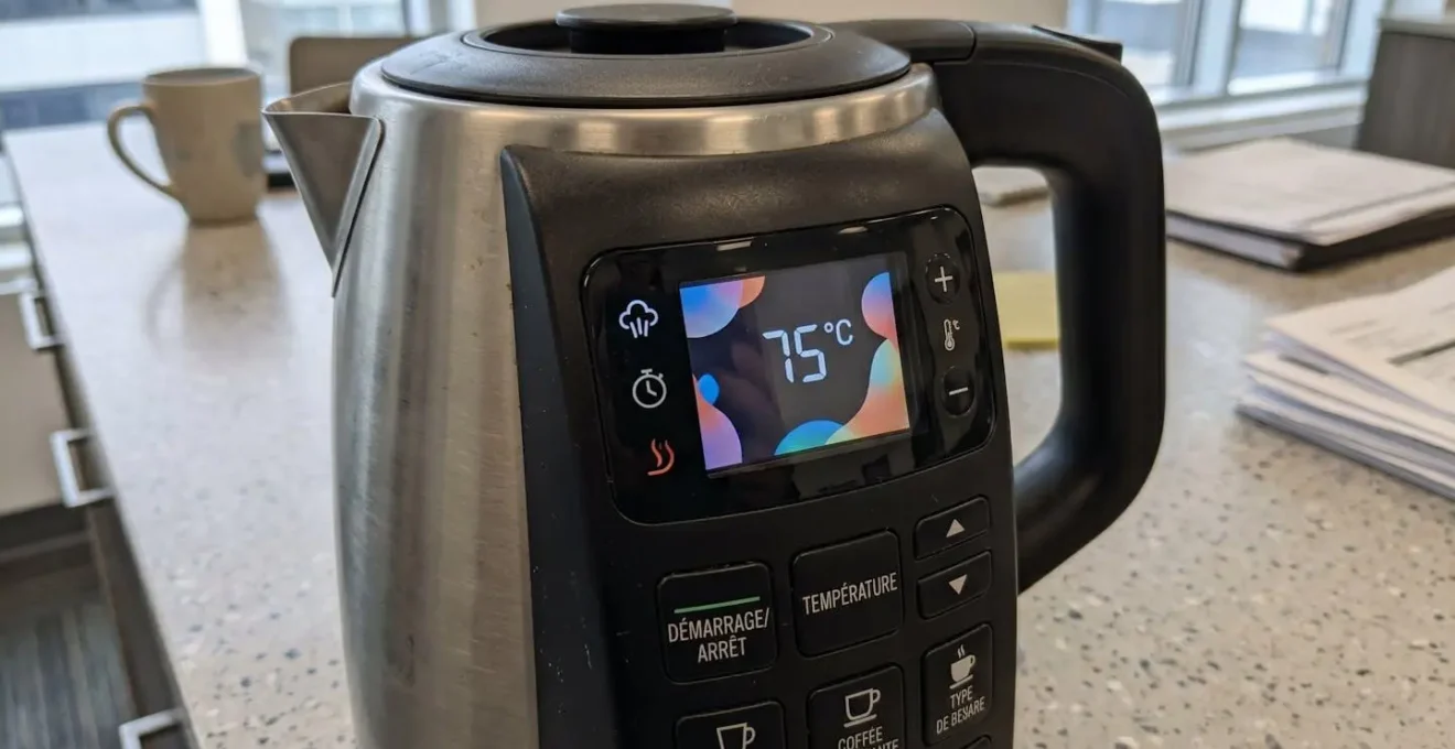 Gros plan sur l'écran tactile d'une théière électrique moderne avec affichage numérique complètement flouté, posée sur un plan de travail lumineux